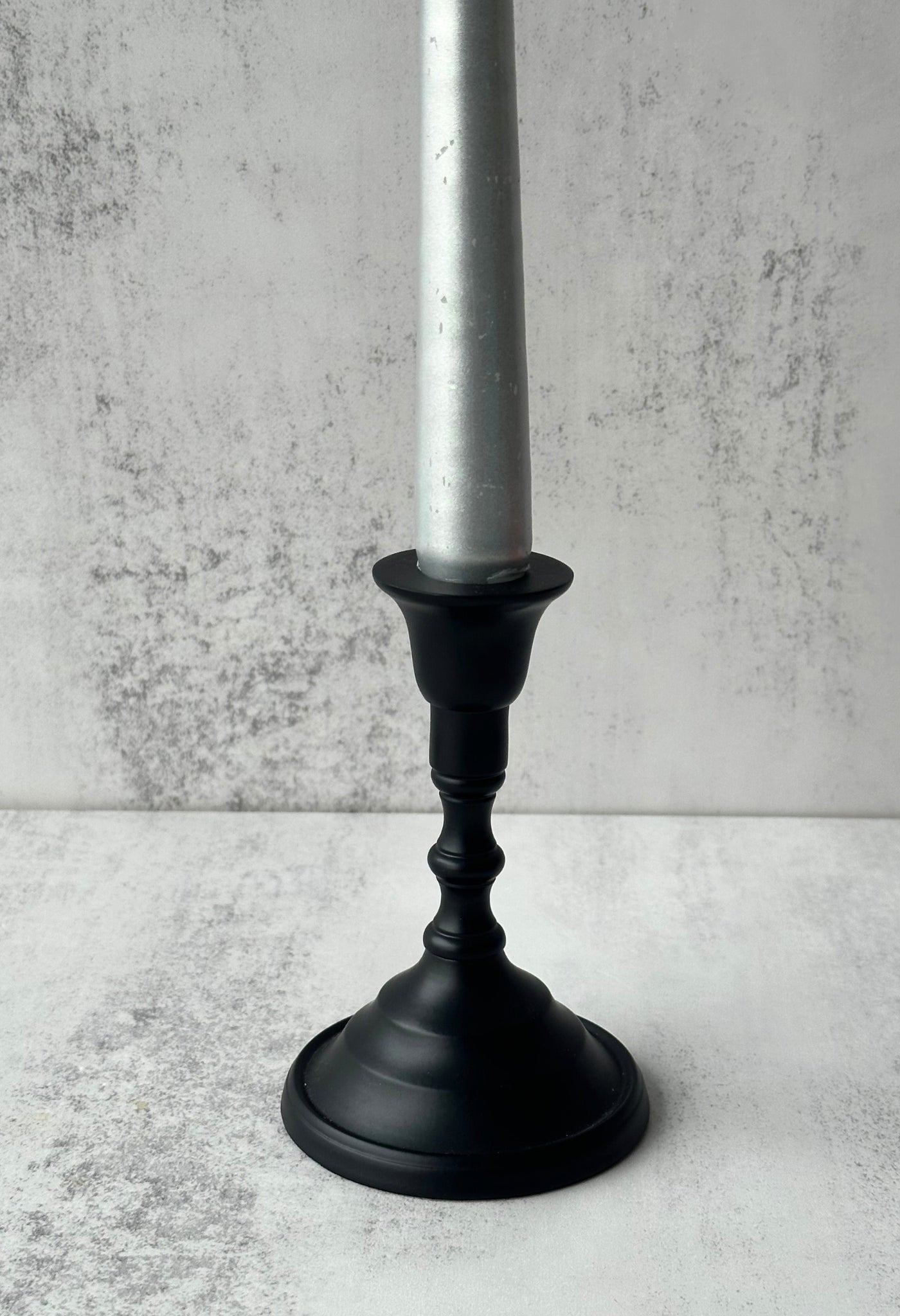 Matte black Tanna sculptural candle holder with a traditional turned stem and silver taper candle.
