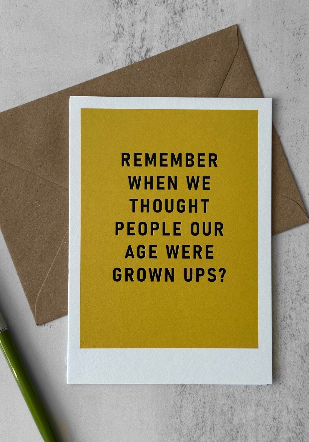 Greeting card with text 'Remember when we thought people our age were grown ups?' on a yellow background with a brown envelope.