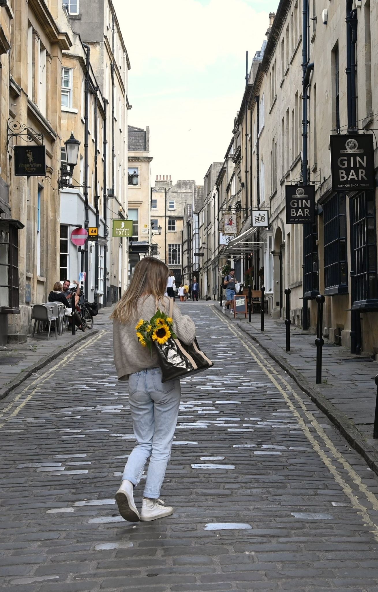A person walking down a street carrying a small gunmetal gray Uashmama tote bag with a floral pattern.