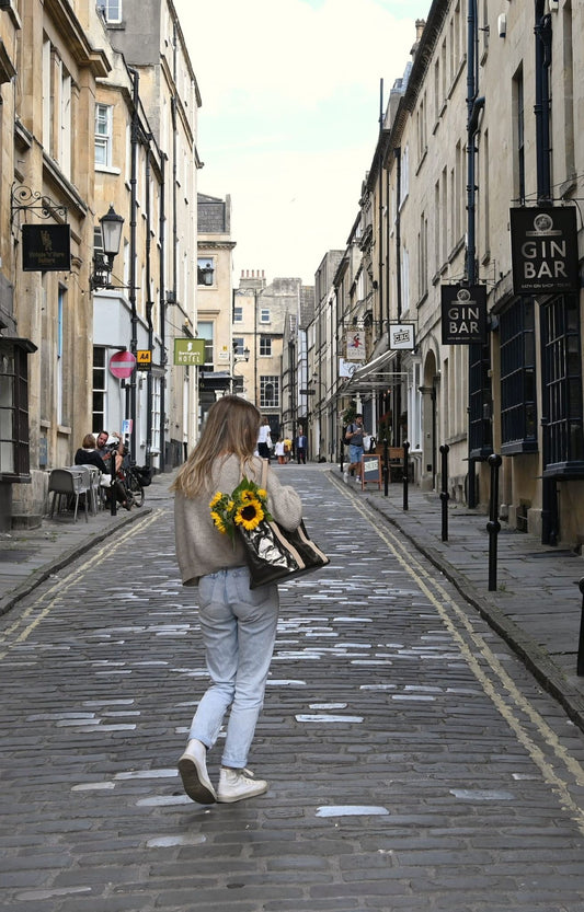 A person walking down a street carrying a small gunmetal gray Uashmama tote bag with a floral pattern.