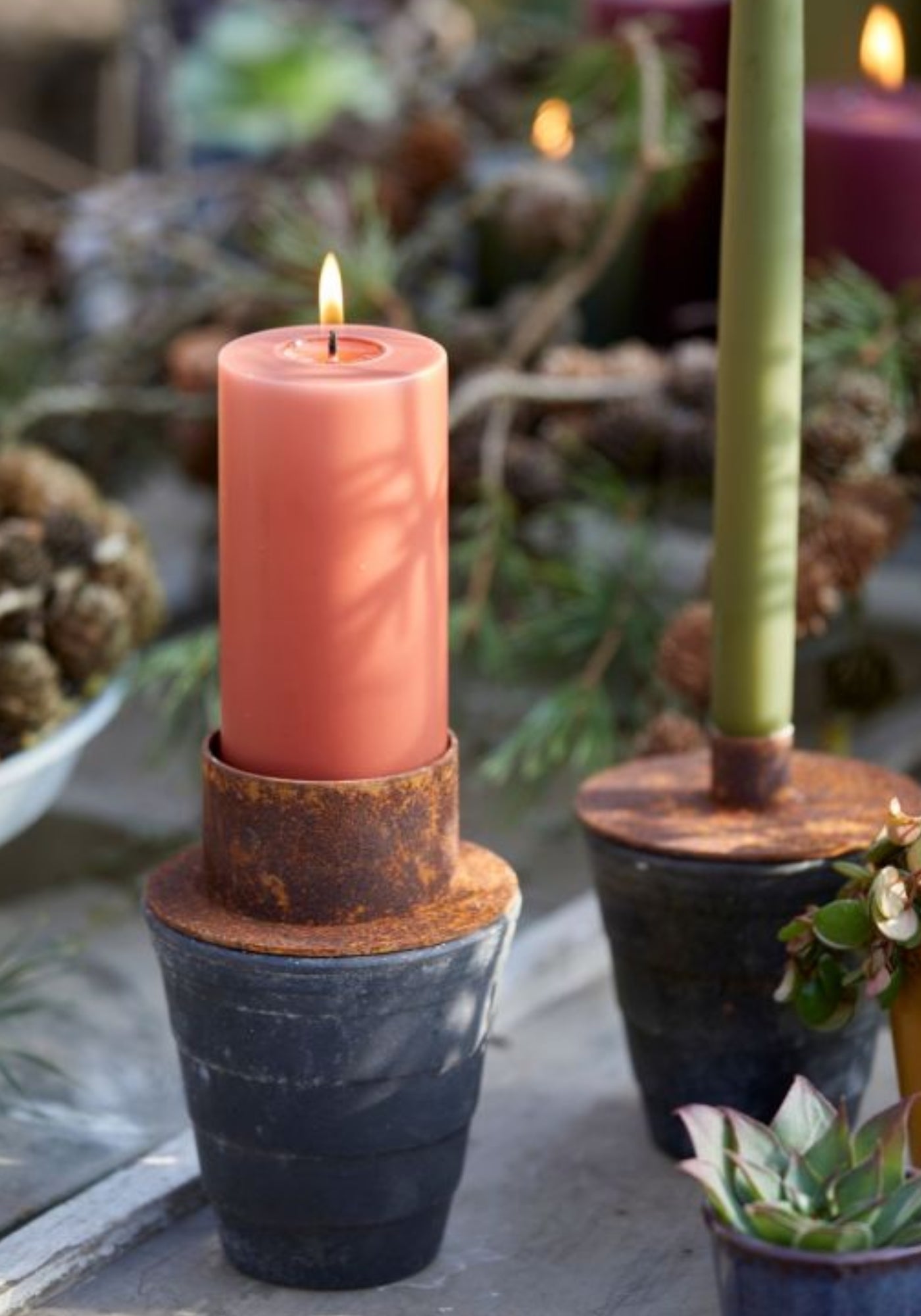 Close-up of rustic metal candle holder with rusted collar and terracotta pillar candle.