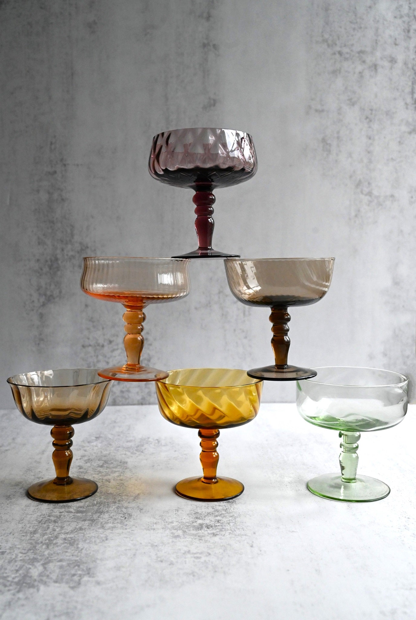 Six multicoloured, textured Art Nouveau champagne coupe glasses stacked in a pyramid.