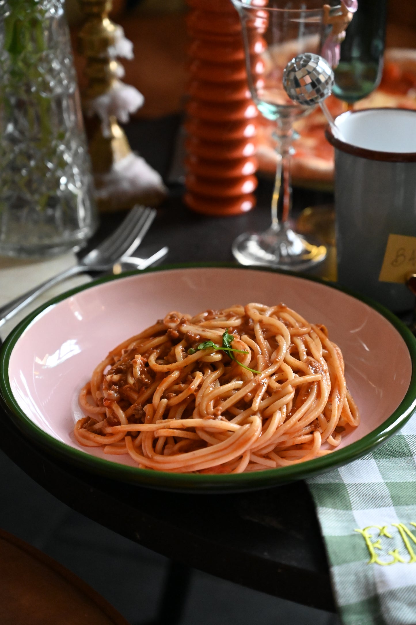 Blush pink enamel pasta plate serving spaghetti with green rim detail.