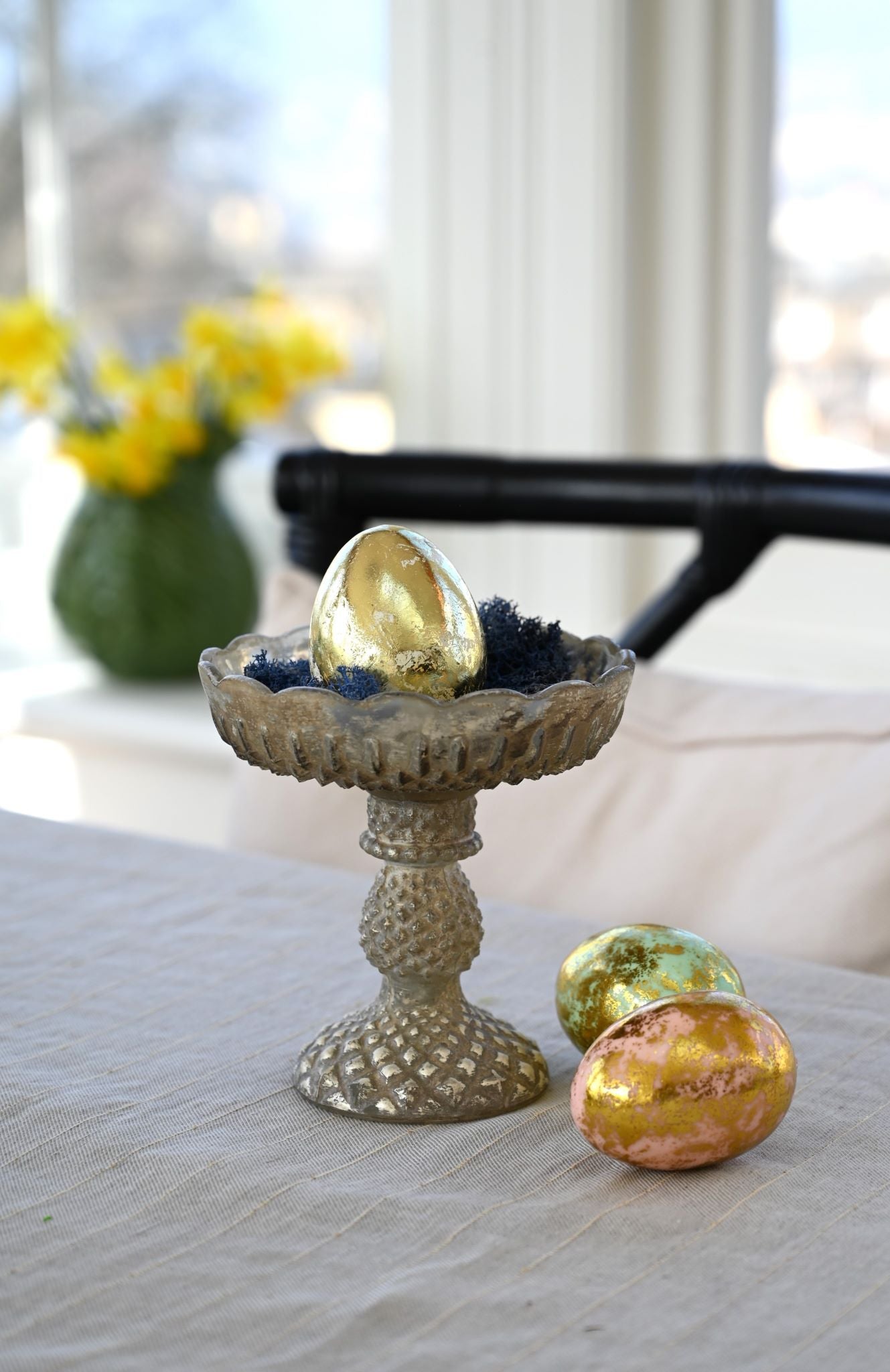 Small distressed antique glass pedestal dish used to display golden Easter eggs.