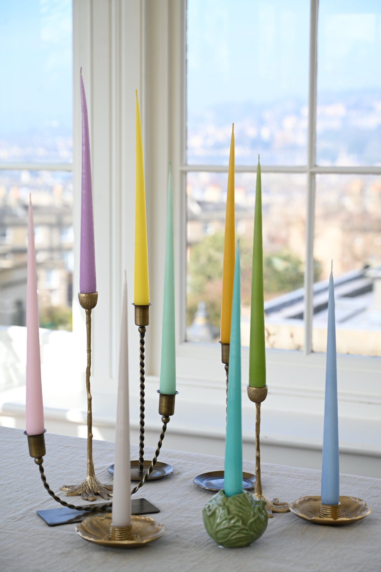 Collection of vibrant, long lacquer taper candles displayed in vintage brass holders.