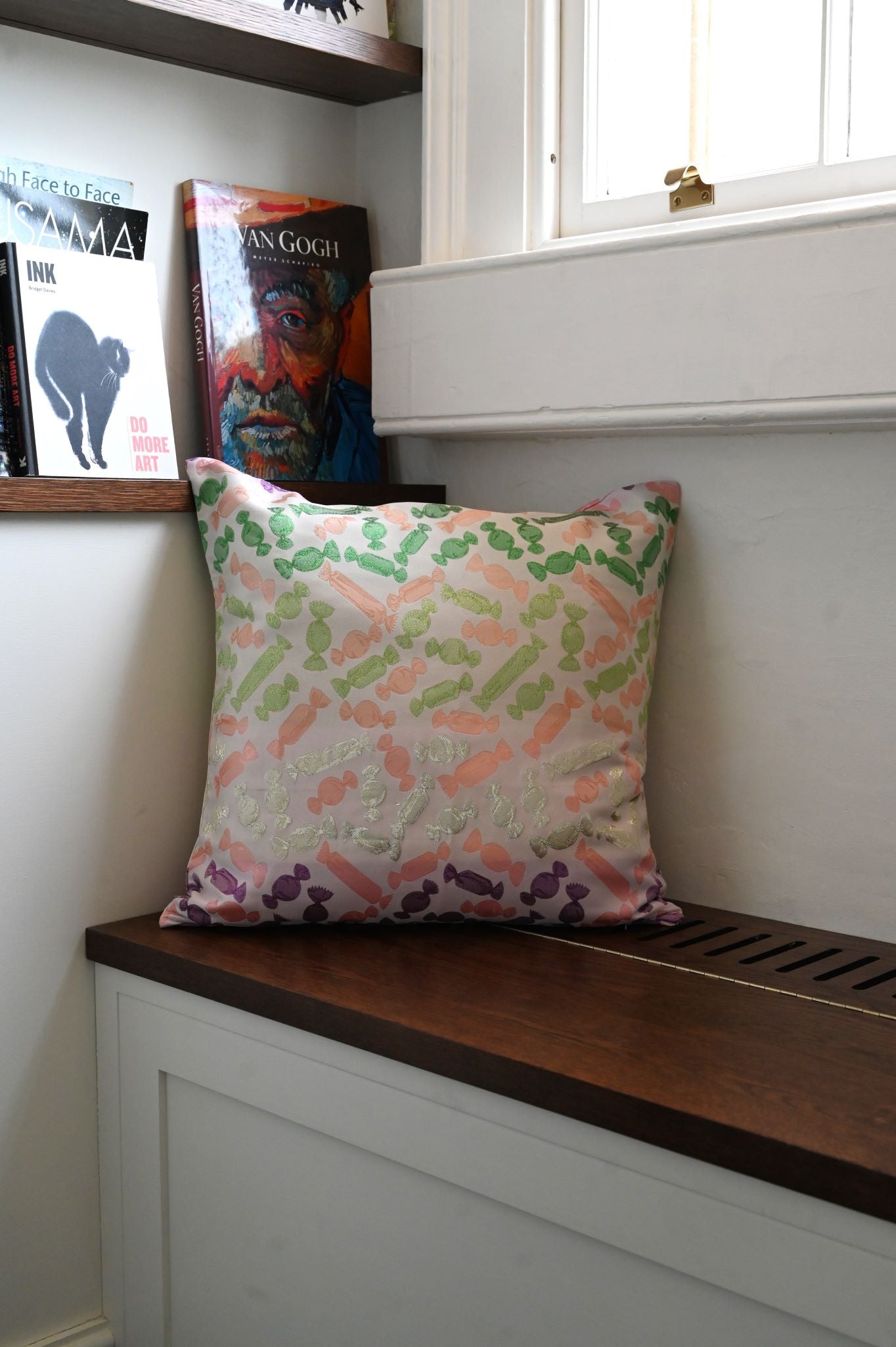 Square pink throw cushion with whimsical repeating green and purple candy pattern.