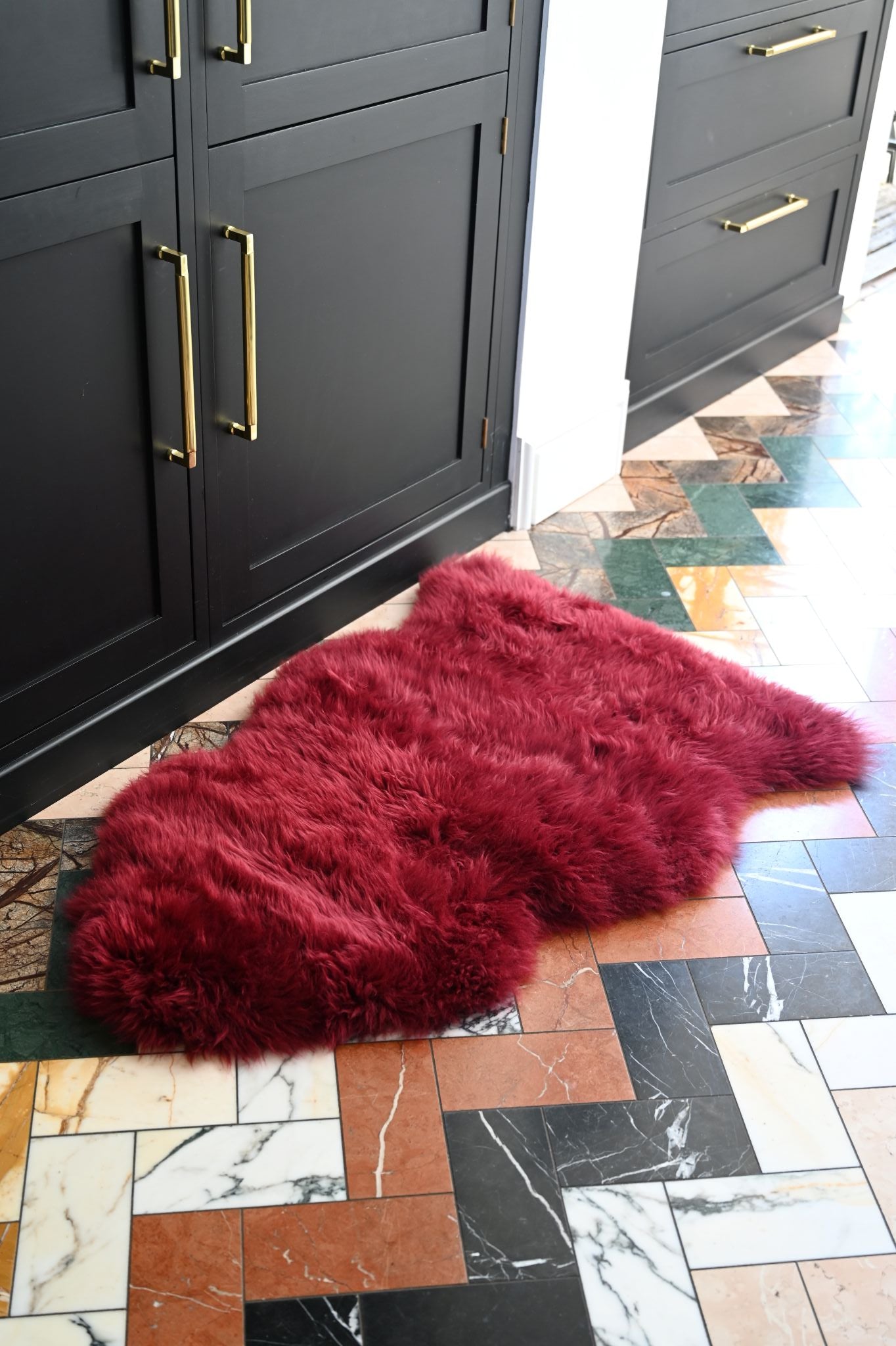 Red fur rug on a kitchen floor with gray cabinets and marble tiles.