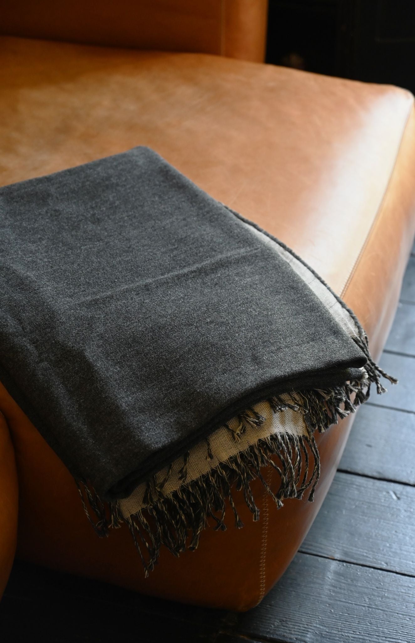 Gray blanket with fringes draped over a brown leather chair.