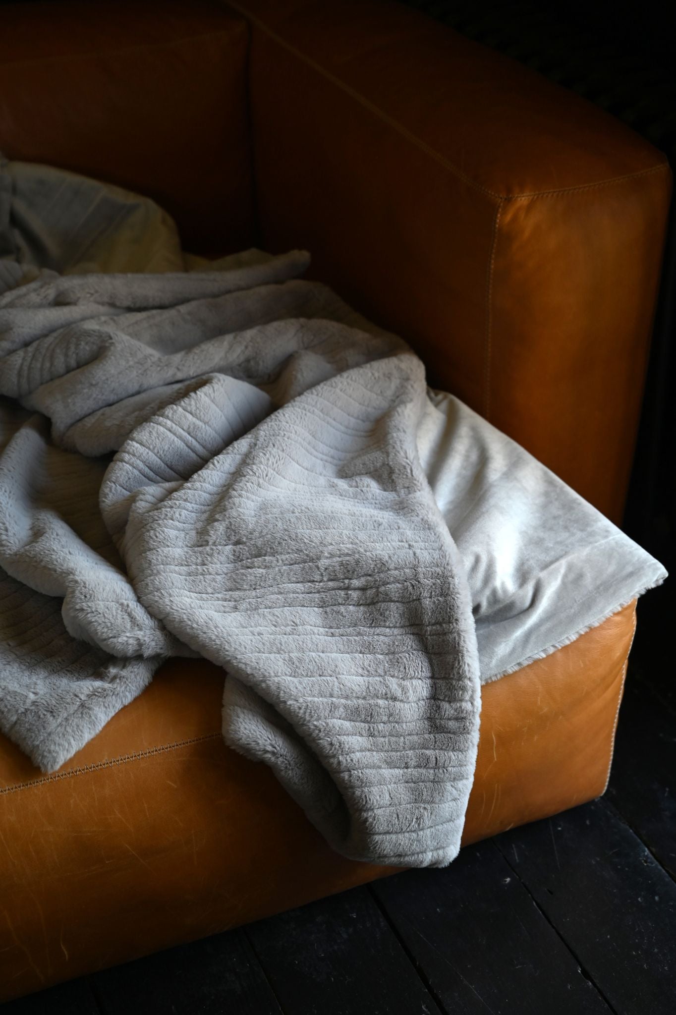 Pearl grey super soft teddy throw blanket draped over a cognac leather armchair.