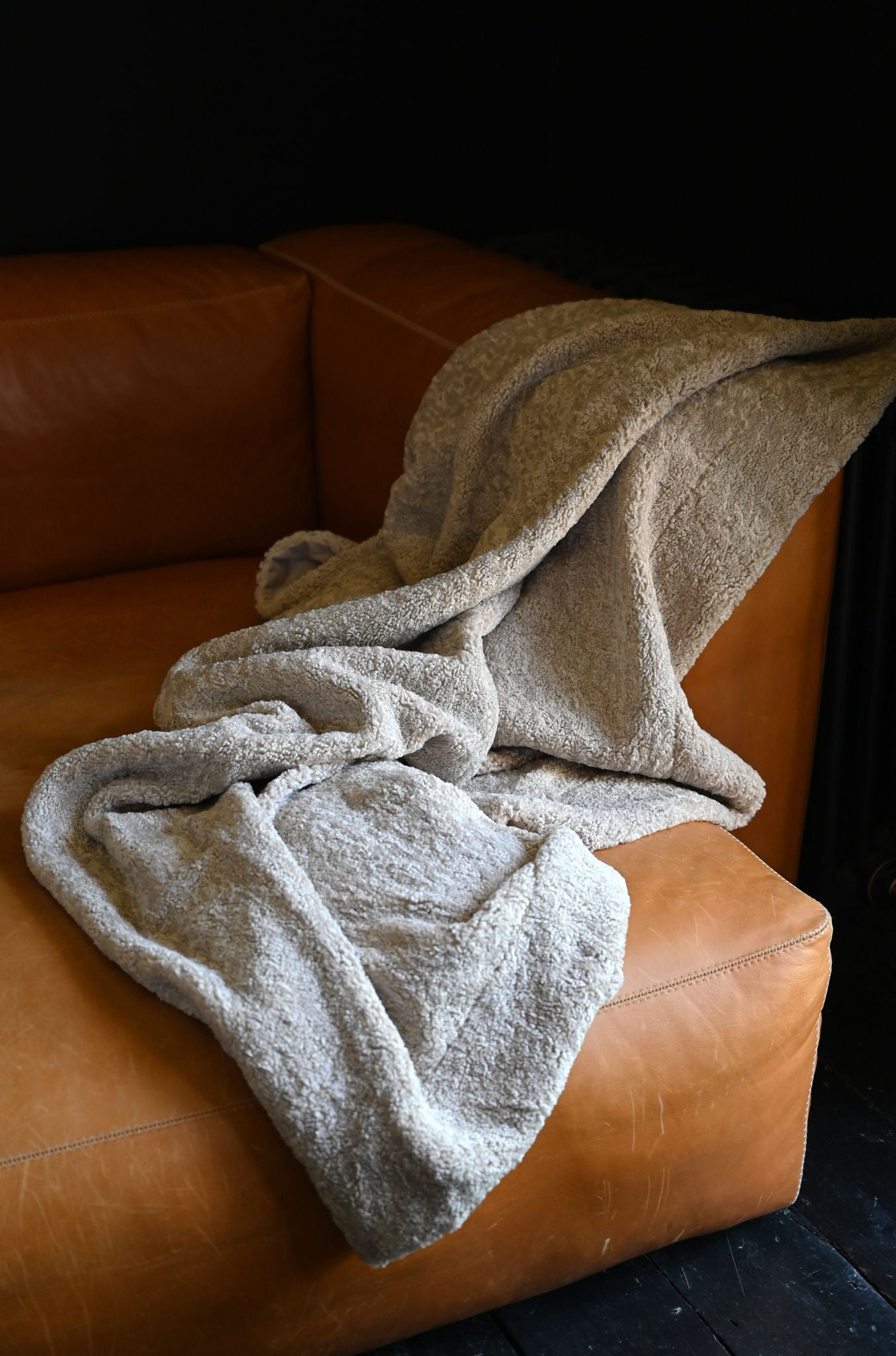 Taupe fluffy bouclé throw blanket draped over a warm leather sofa.