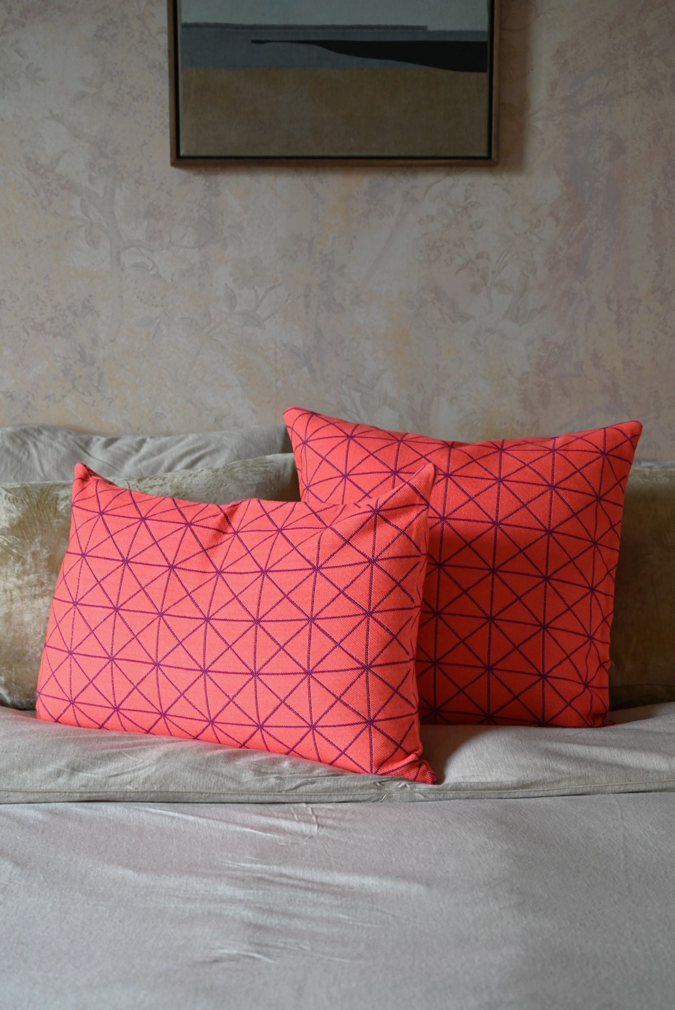 Two geometric-patterned orange pillows on a gray sofa against a beige wall.