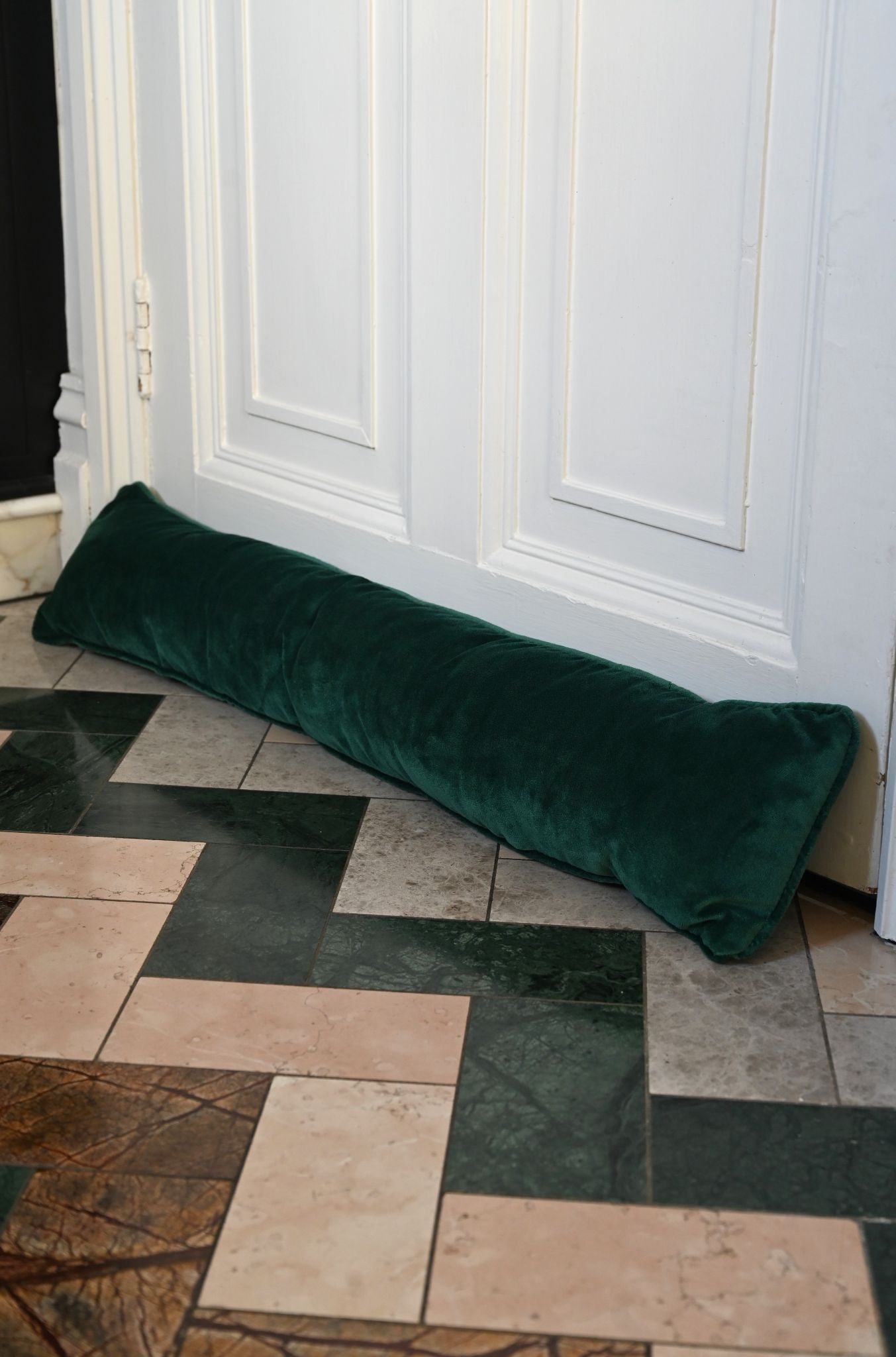 Handmade forest green velvet draught excluder placed against a white door.