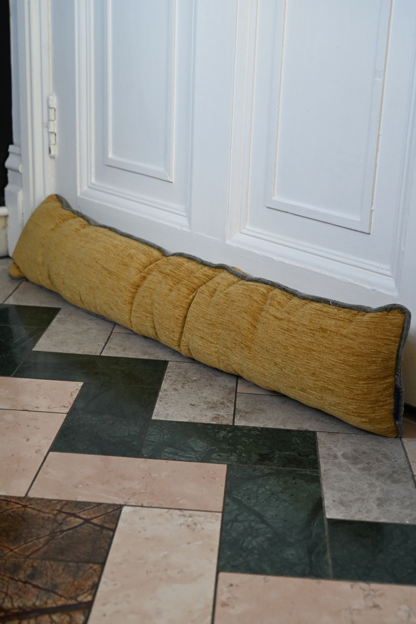 Mustard yellow ribbed chenille draught excluder placed against a white door.
