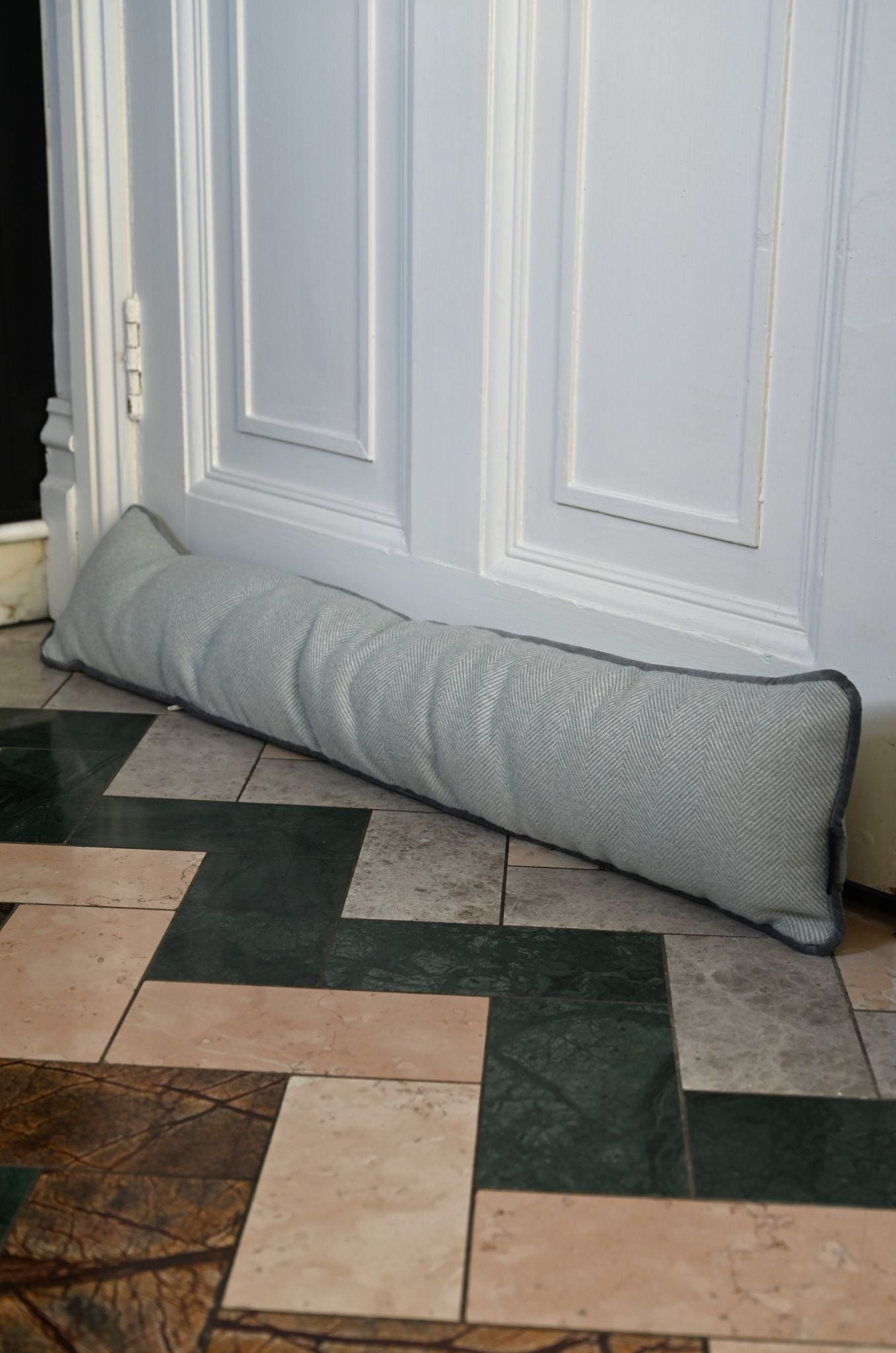 Handmade duck egg blue herringbone draught excluder against a white door frame.