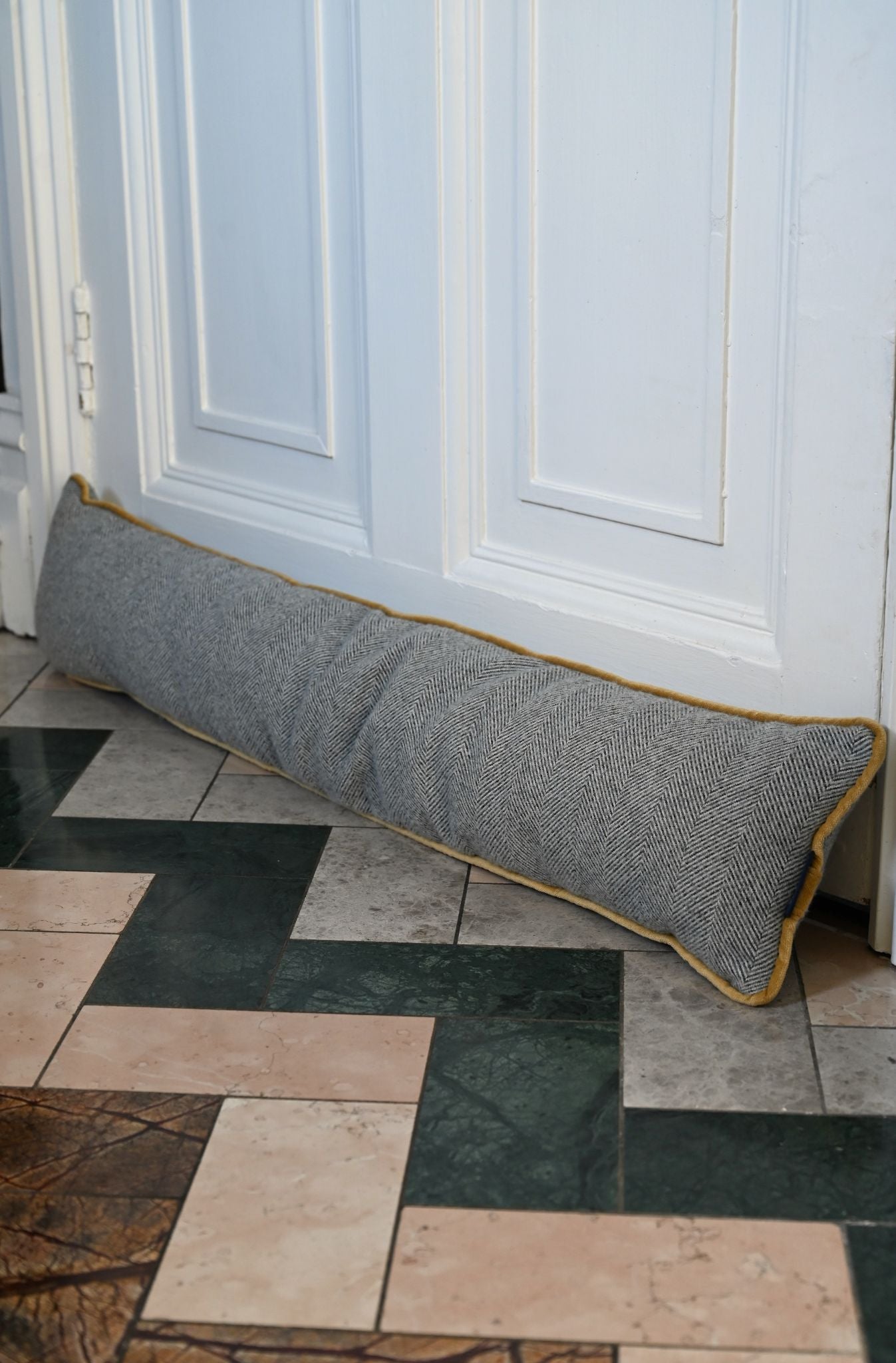 Handmade grey herringbone draught excluder with bright mustard yellow piping against a white door.