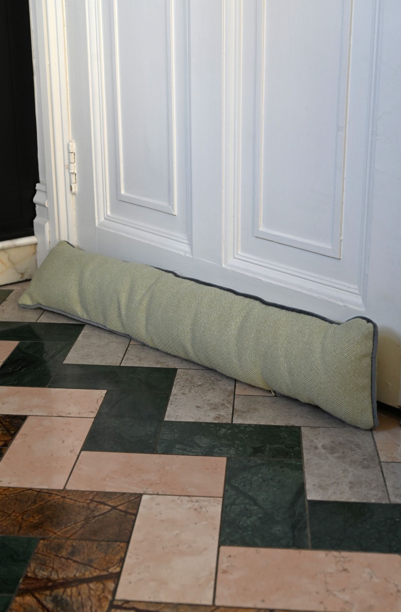 Sage green herringbone draught excluder placed against a white interior door.