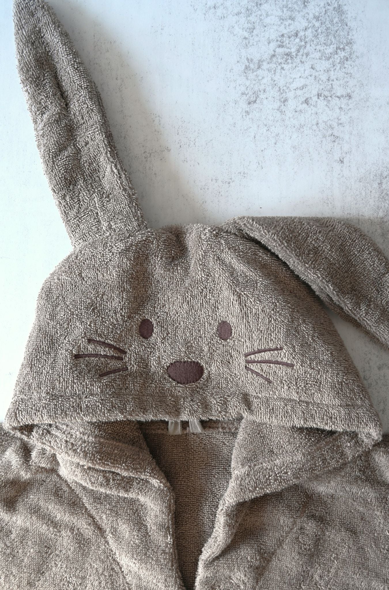Brown towel with bunny ears and face on a light gray background