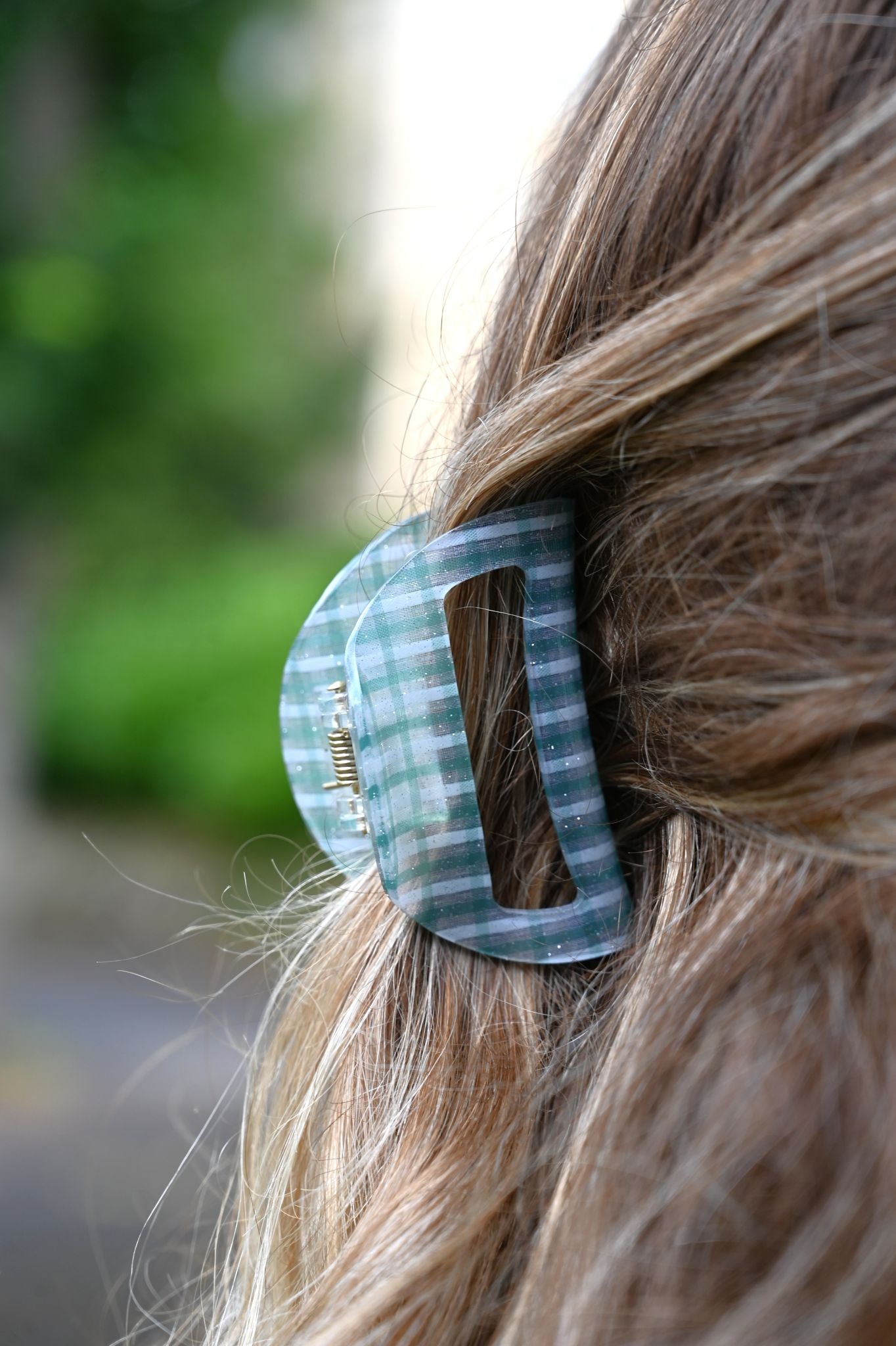 Close-up of a checkered hair clip in blonde hair with a blurred green background