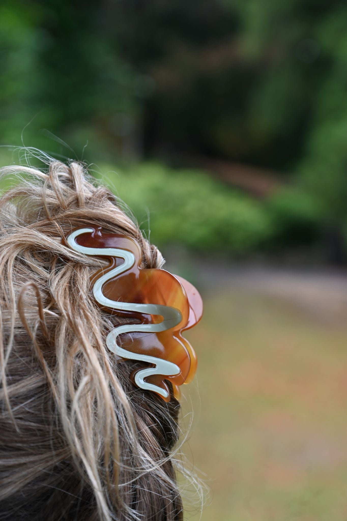 Hair clip with wavy design in hair against a blurred natural background