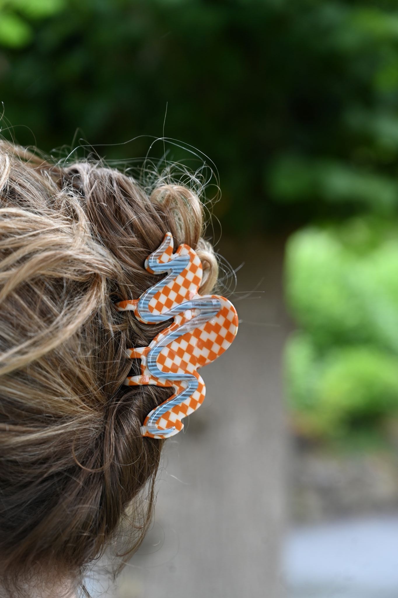 Hair tie with orange and blue pattern on a braided hair against a blurred green background