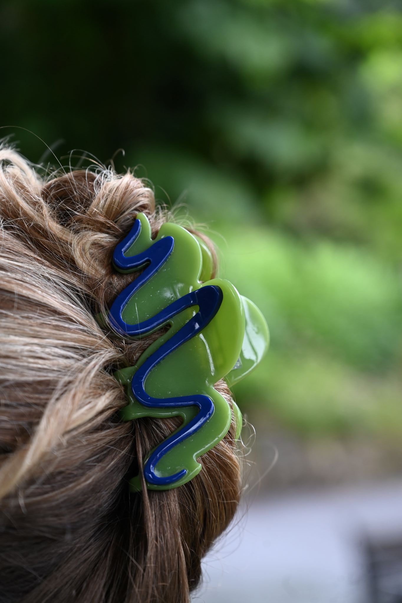 Green hair clip with blue accents in a person's hair against a blurred green background