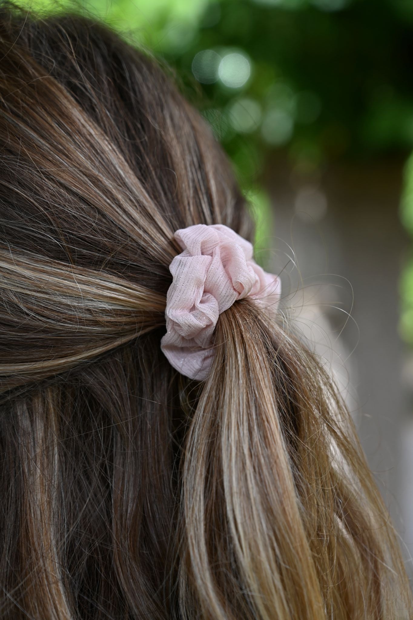 Close-up of a pink scrunchie in brown hair with a blurred green background