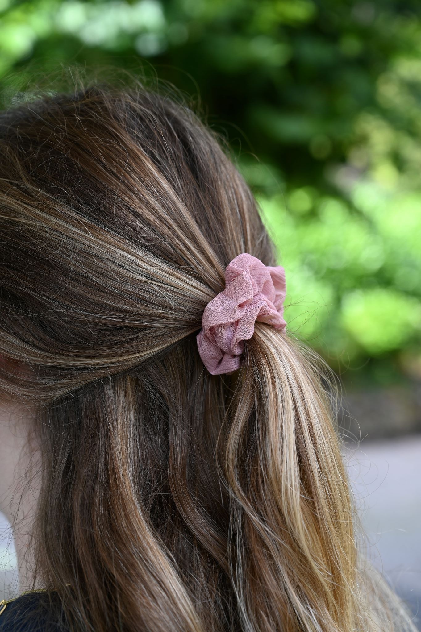 Close-up of a pink scrunchie in a person's hair with a blurred green background