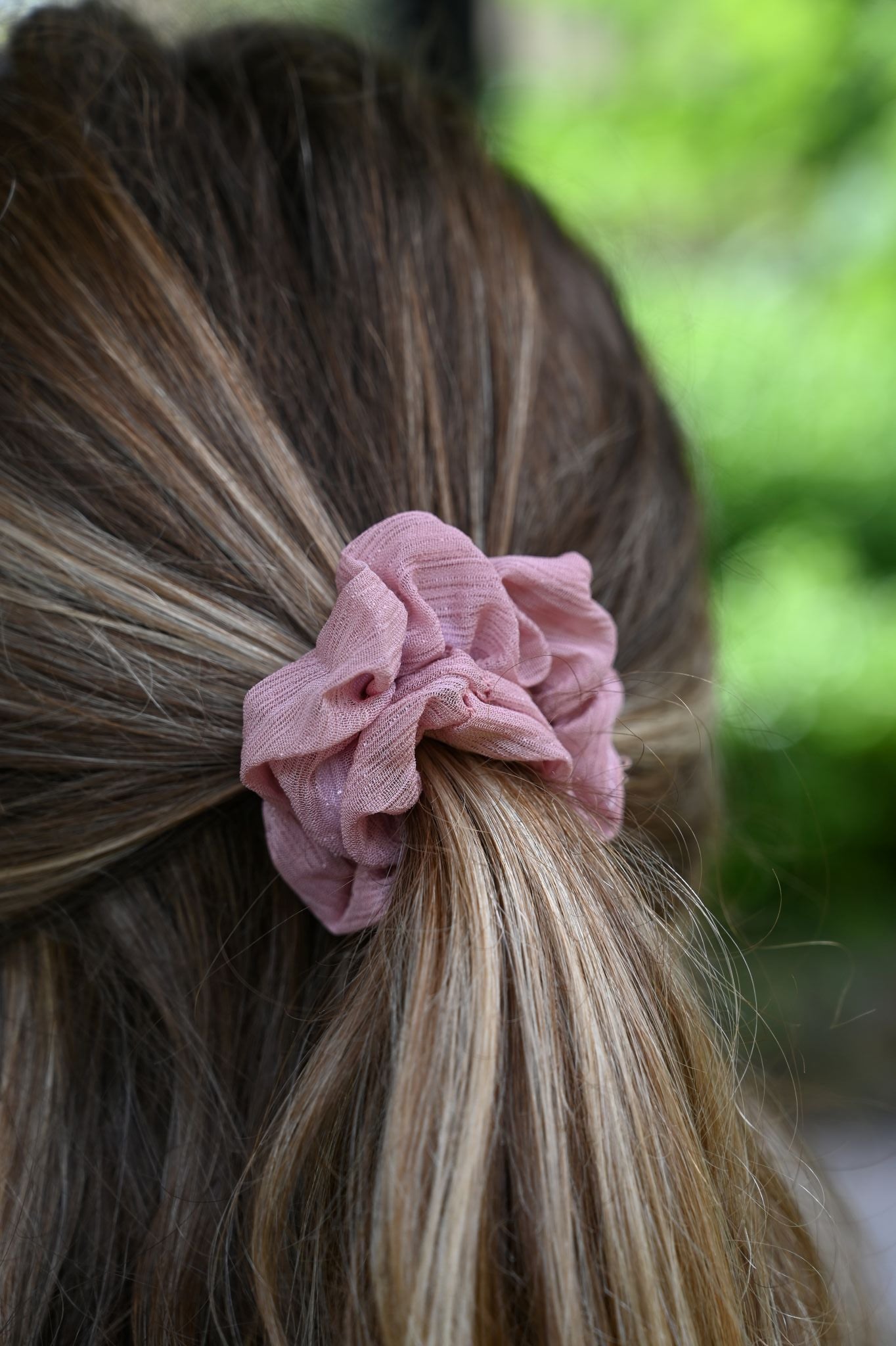 Close-up of a pink scrunchie in a person's hair with a blurred green background