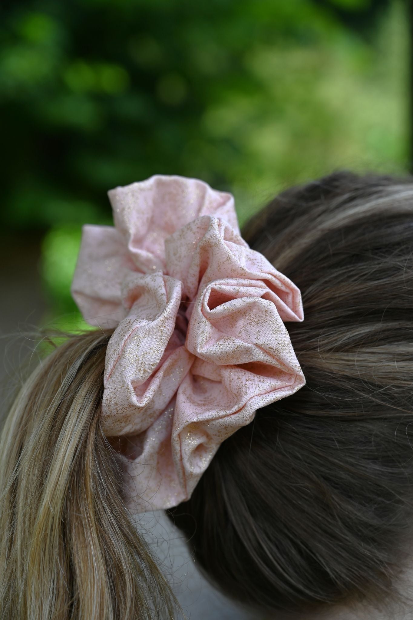 Pink scrunchie in a person's hair with a blurred green background