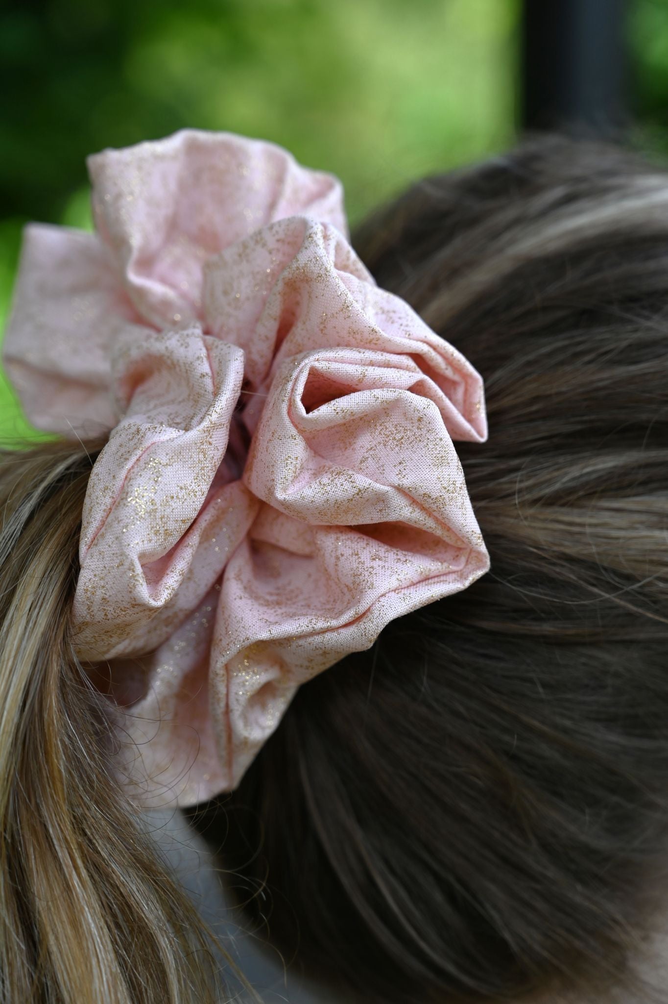 Pink scrunchie on a person's hair against a blurred green background