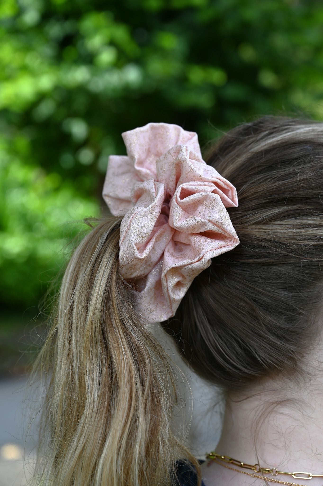 Pink scrunchie in a person's hair with a blurred green background