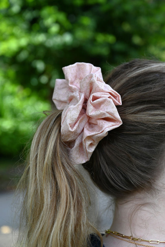 Pink scrunchie in a person's hair with a blurred green background