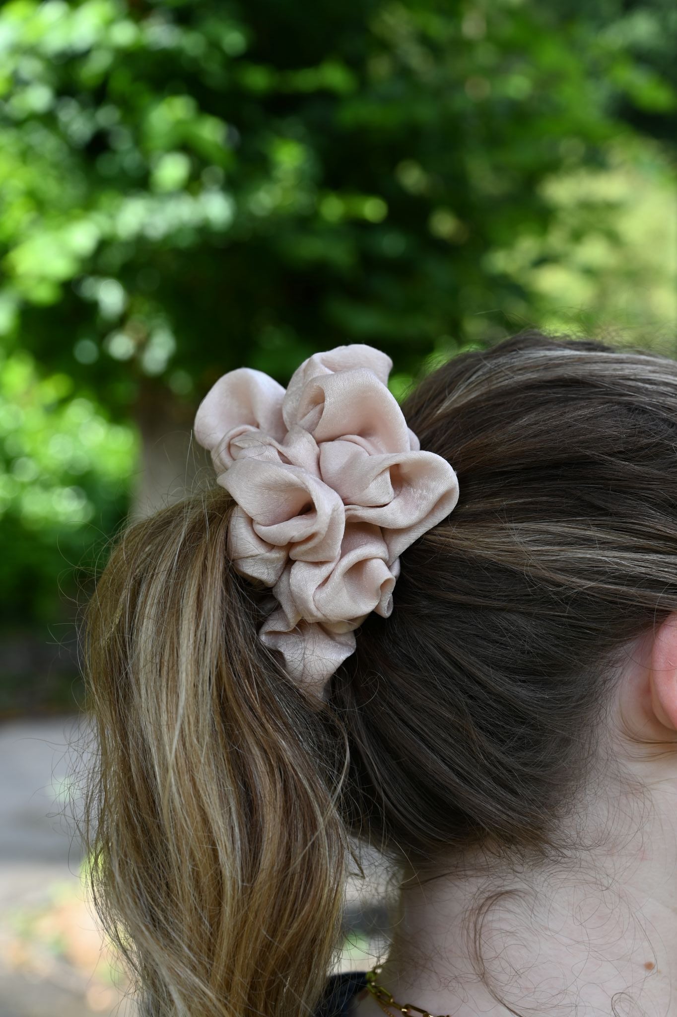 Close-up of a beige floral hair scrunchie on a person's head with a blurred green background