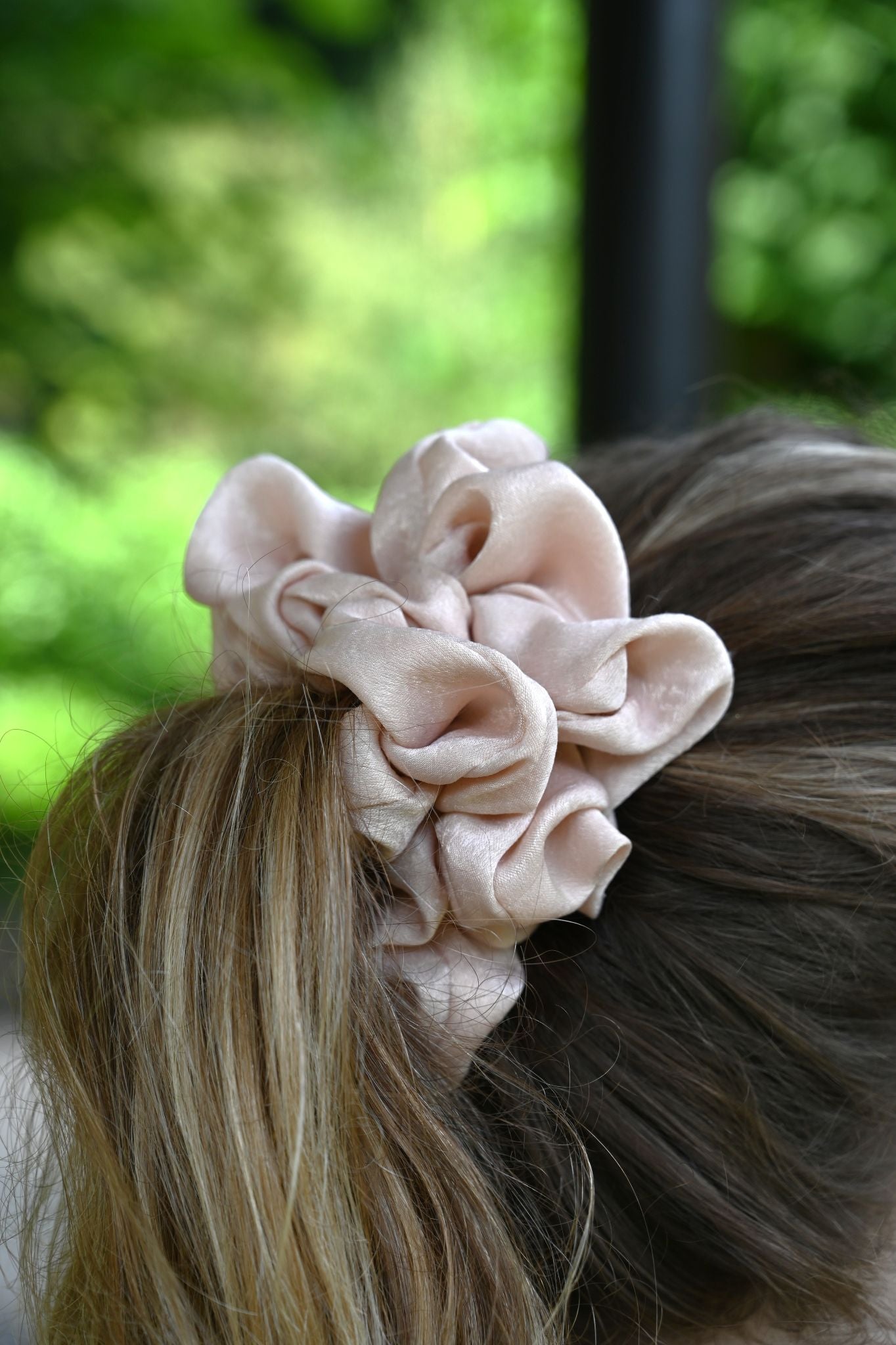 Pink scrunchie on a person's hair with a blurred green outdoor background
