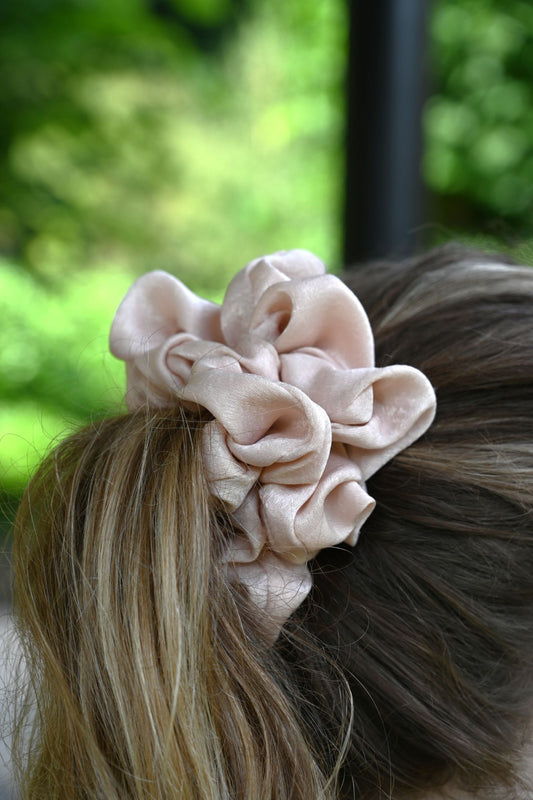 Pink scrunchie on a person's hair with a blurred green outdoor background