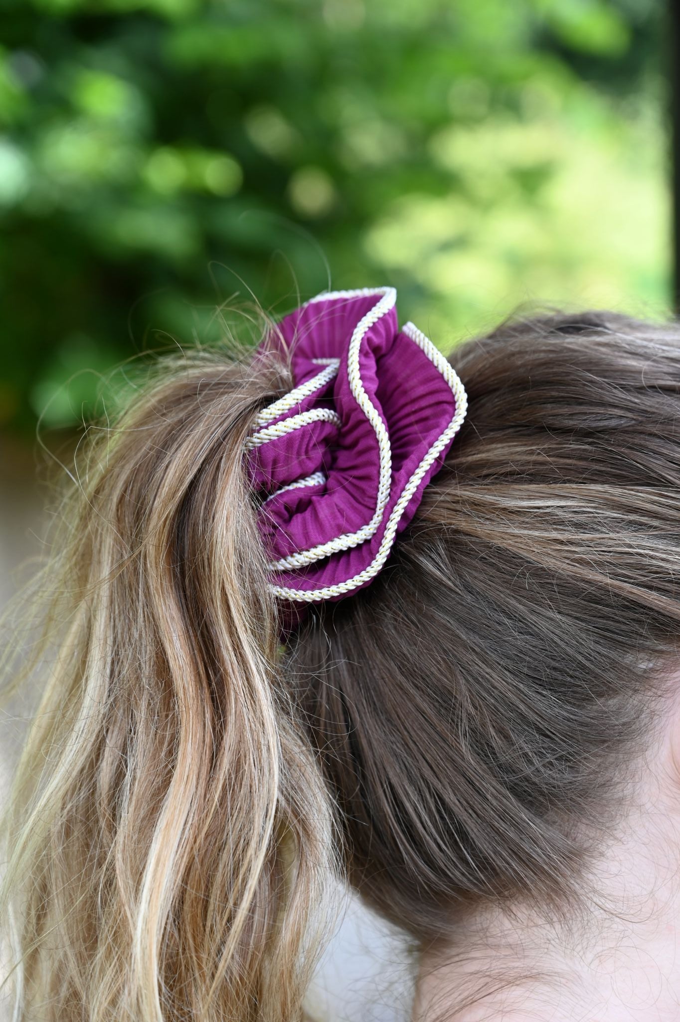 Purple scrunchie in a person's hair with a blurred green background