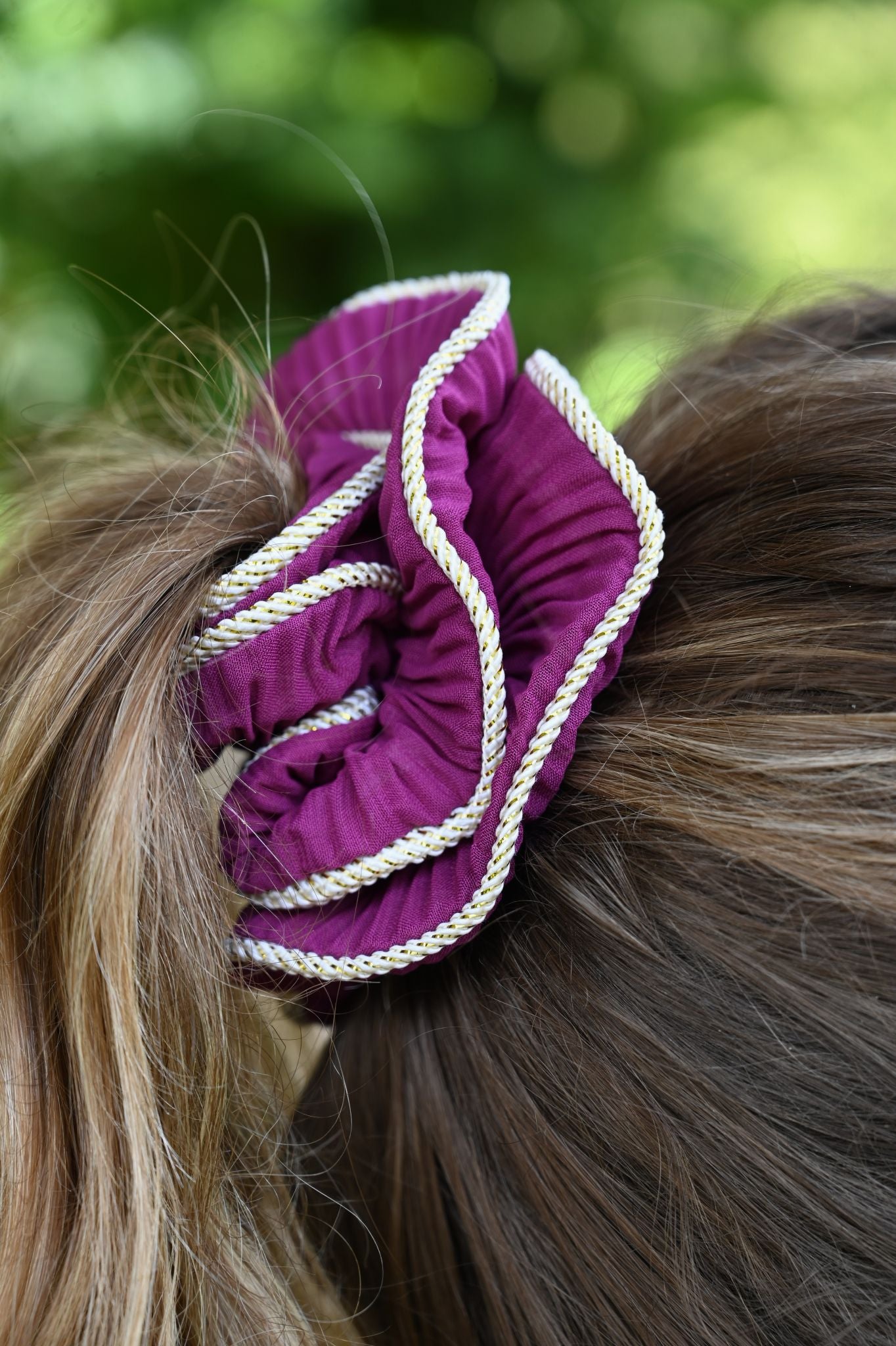 Purple scrunchie with white cord in hair against a blurred green background
