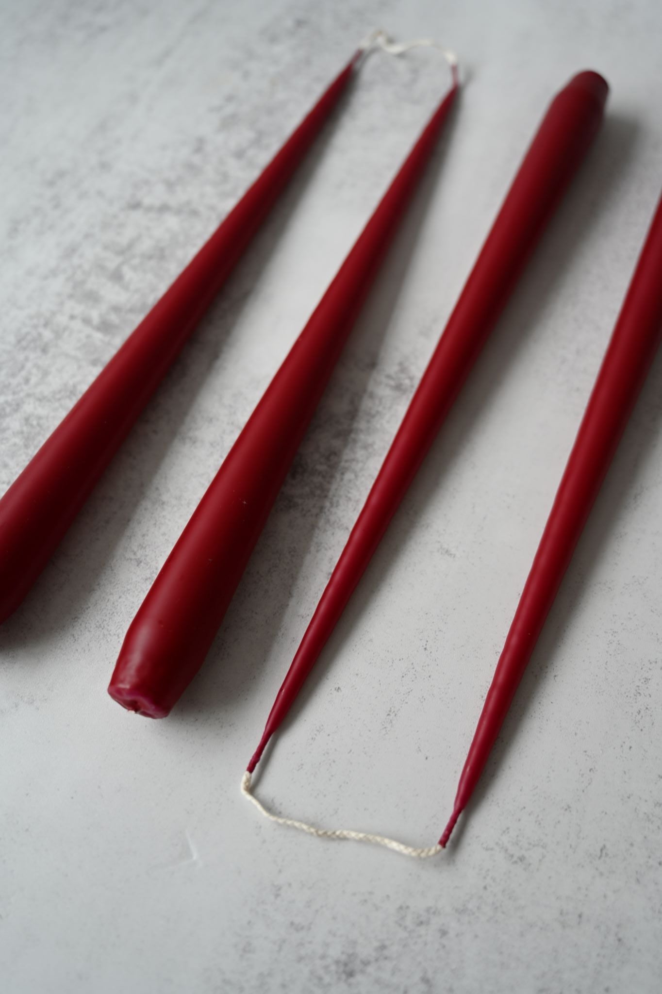 Set of four long, matte wine red taper candles displayed on a grey surface.