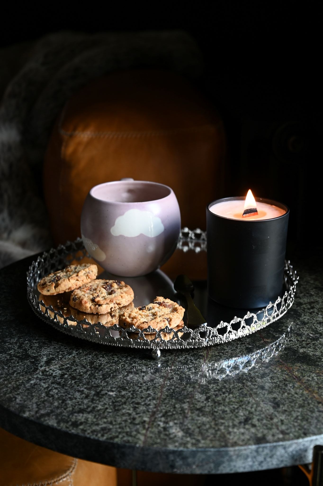 Ornate silver mirrored round tray displaying a candle and cookies on a dark table.