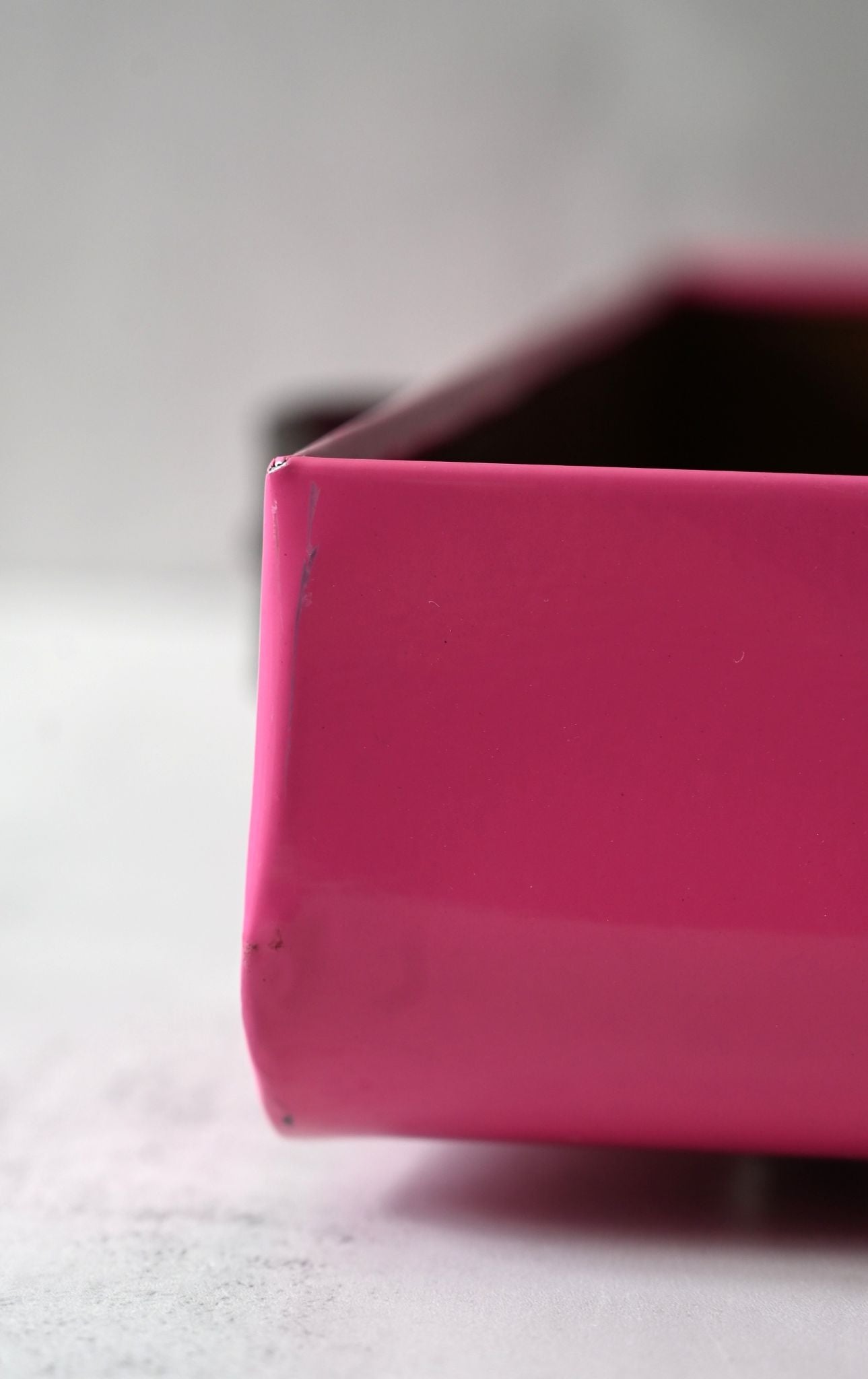 Close-up of a pink rectangular tray on a light gray background. Scratches on the corner of the tray