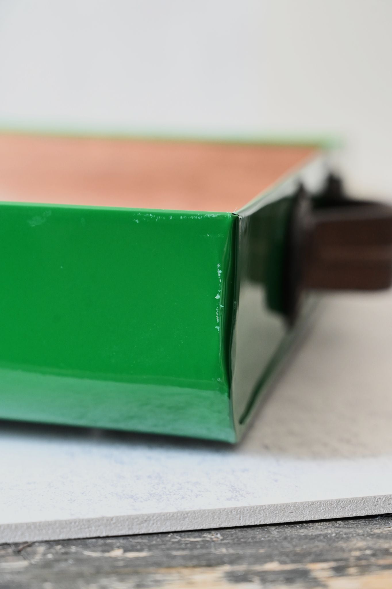 Close-up of a slightly scratched green tray and brown handle on a wooden surface