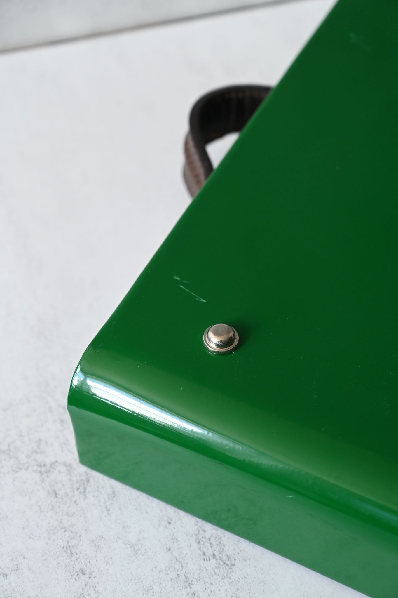Close-up of a green metal tray with a silver button foot on a light gray background