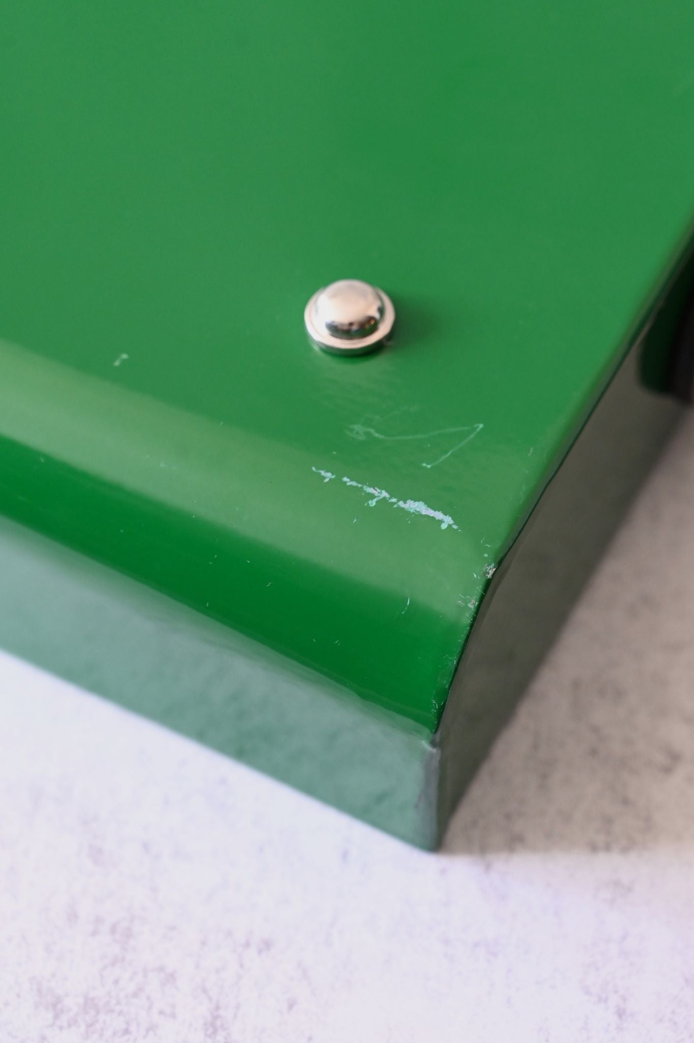 Close-up of a metal button foot on a green tray wth small scrapes