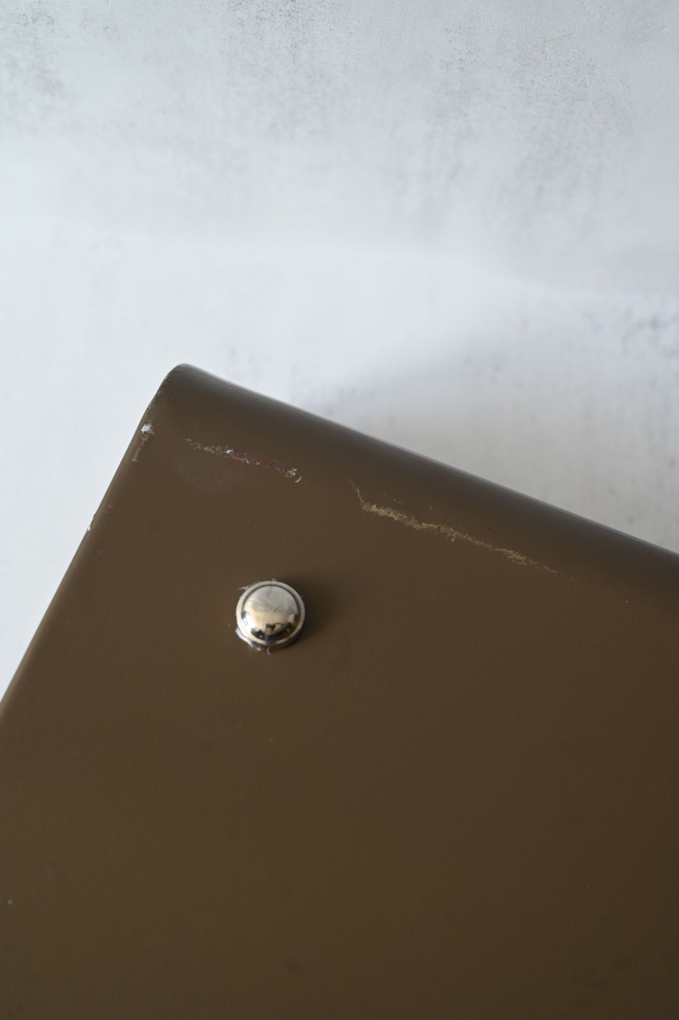 Brown metal tray with a silver button foot on a light gray background. Shows slight damage