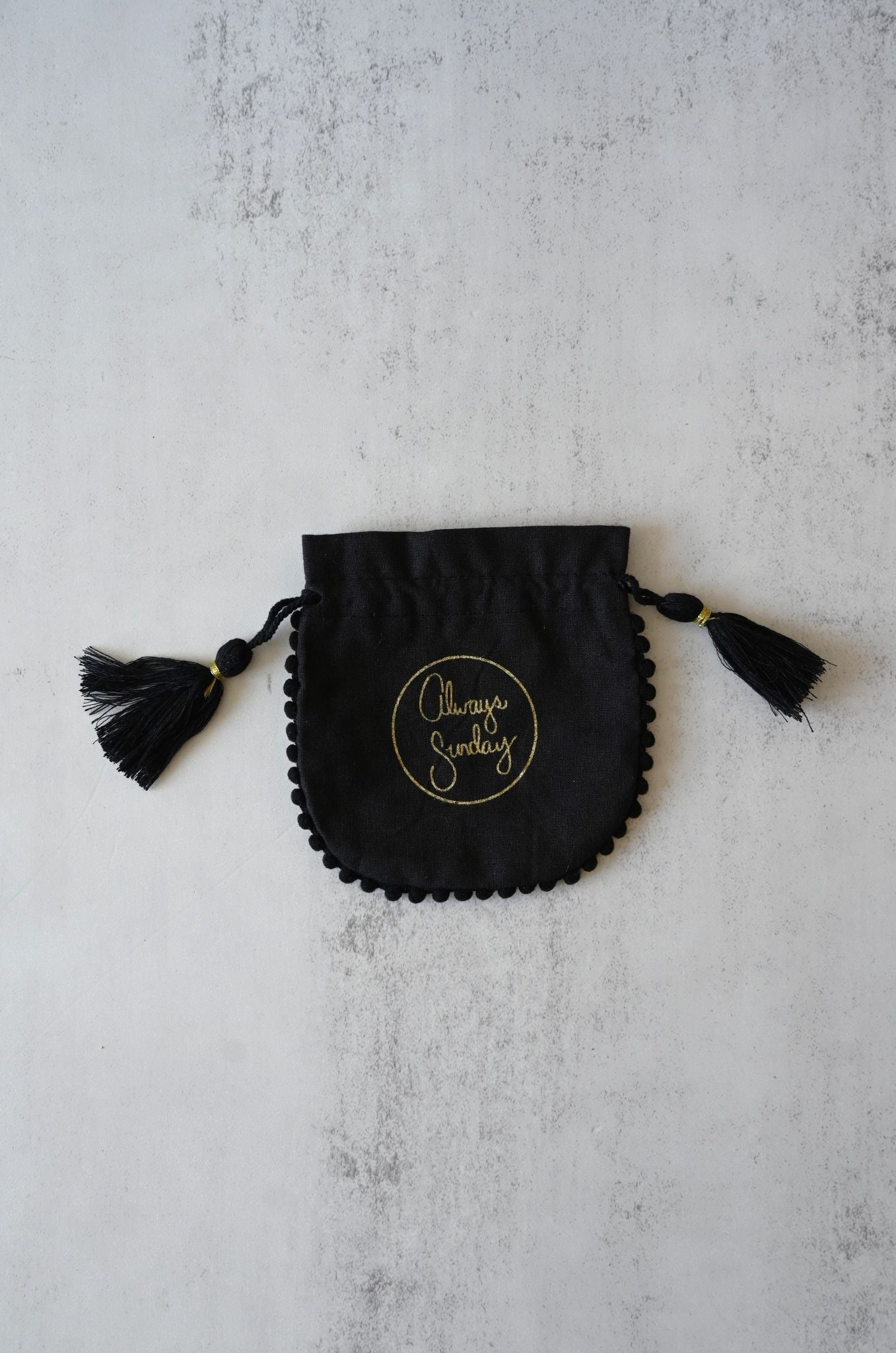 Black drawstring pouch with tassels on a light gray background