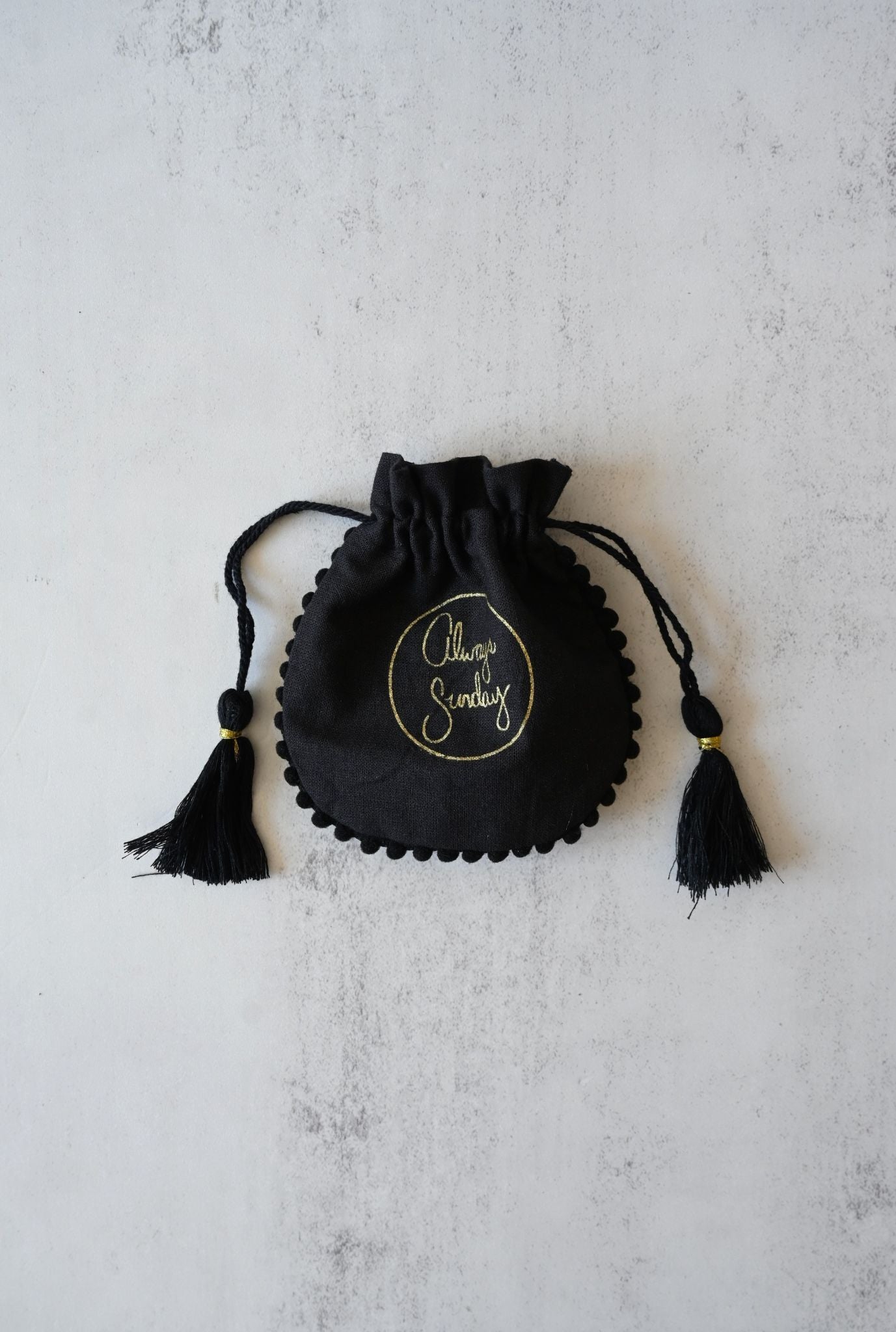Black drawstring pouch with tassels on a light gray background