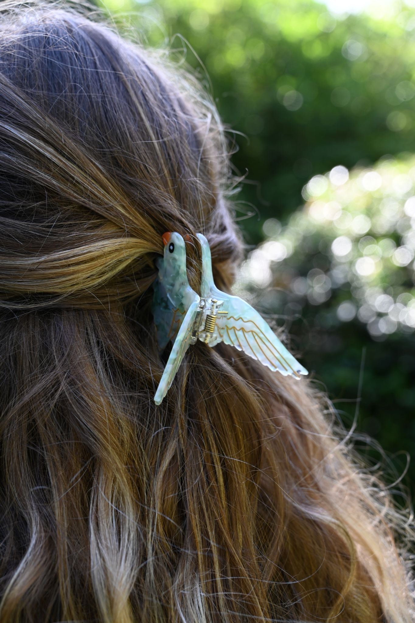 Hair clip with a bird design in a person's hair against a blurred natural background