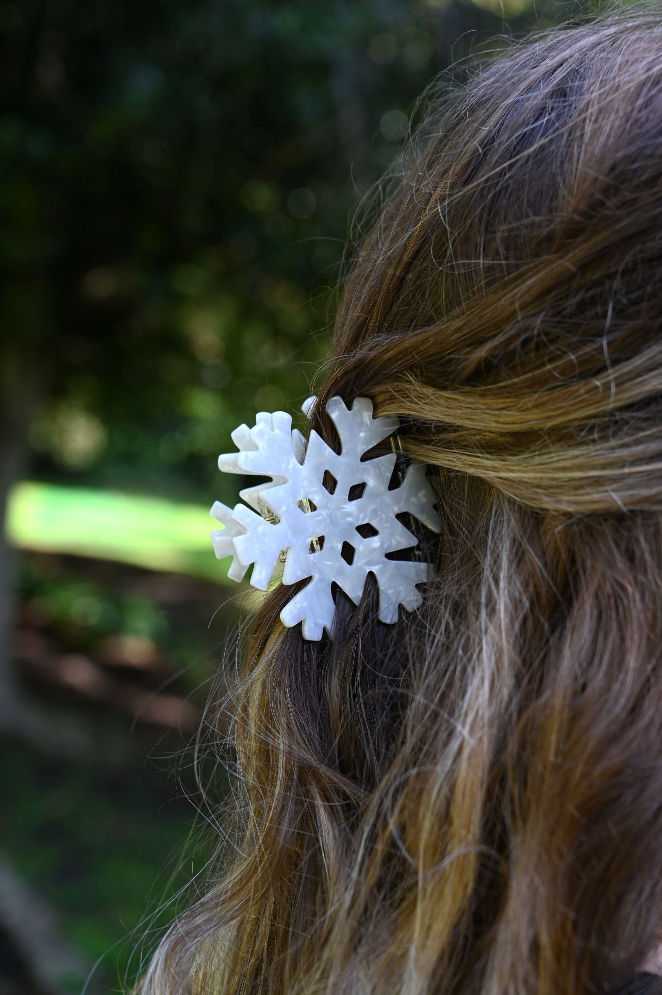 White pearlescent snowflake hair claw securing brown hair outdoors.