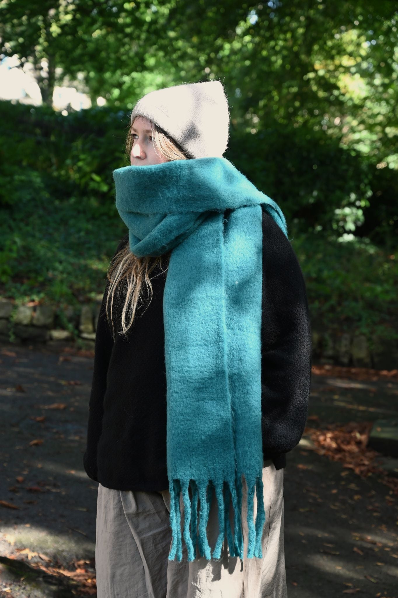 Oversized fuzzy teal scarf worn outdoors with a light grey beanie.