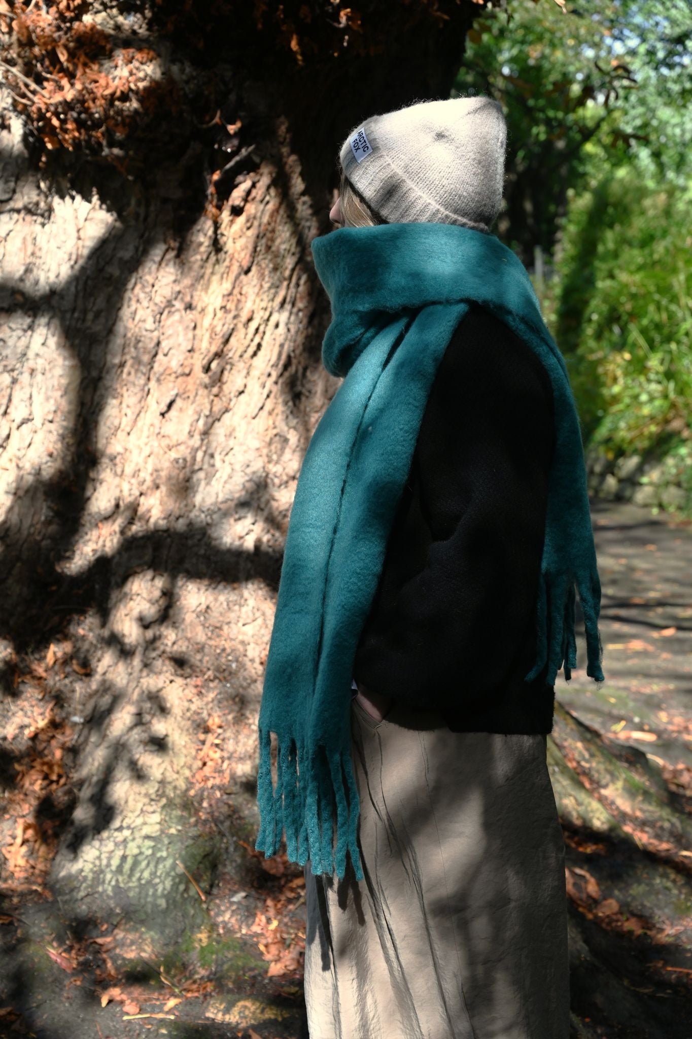 Person wearing a teal scarf standing next to a tree